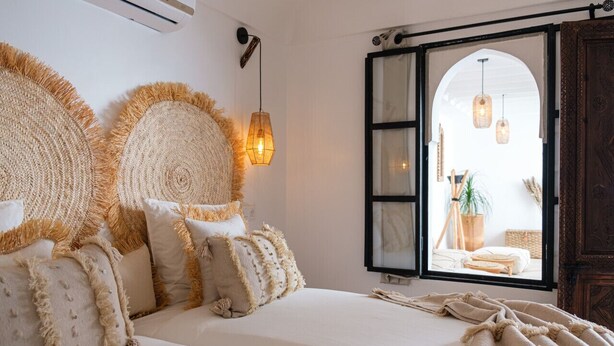Une chambre avec un grand lit, une vue sur l’extérieur par une porte ouverte et un luminaire suspendu.
