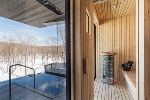 A modern sauna with wooden walls and a glass door, a bench, and a small heater. - Corniche Hirafu (Kutchan)