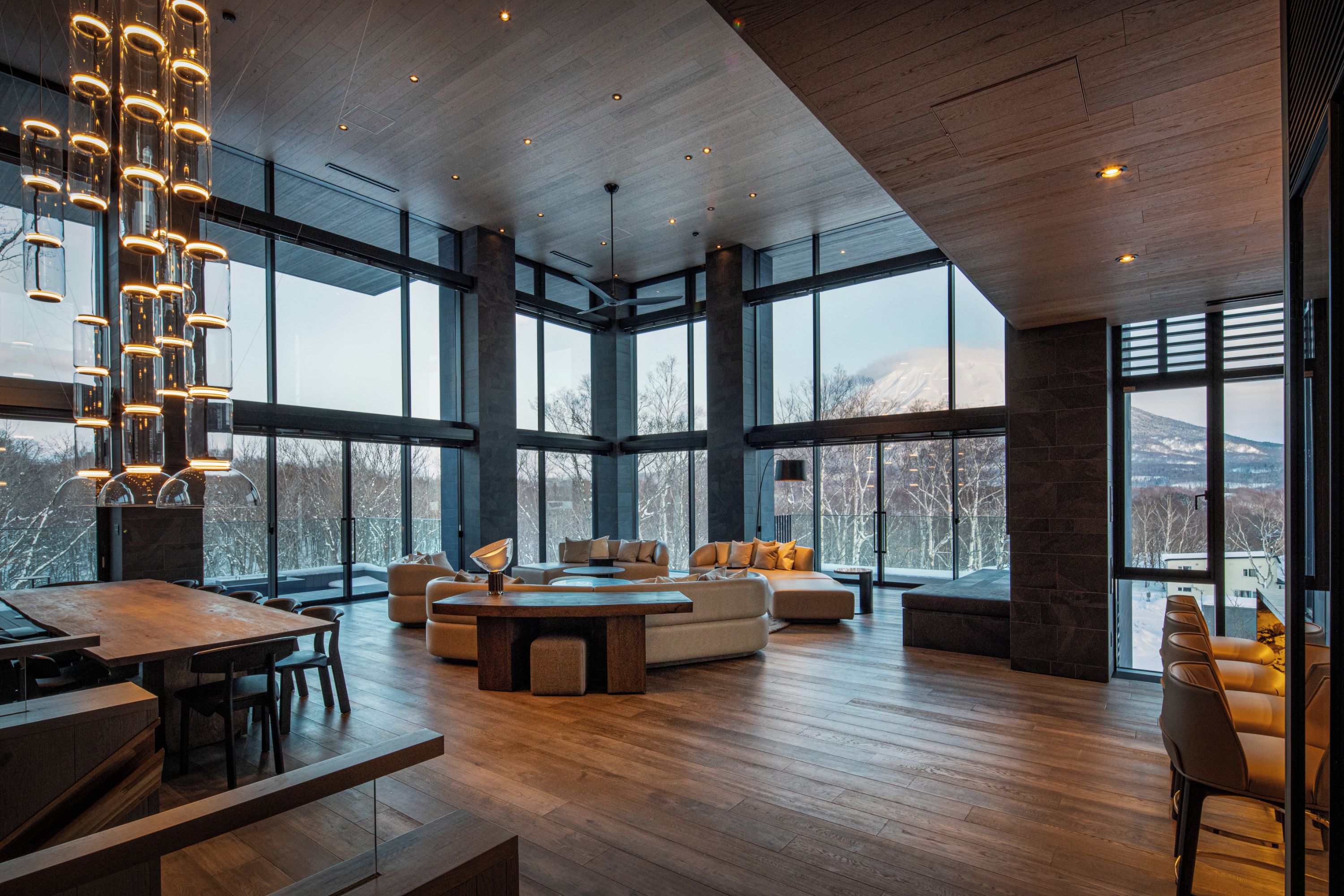 A spacious living area with a large wooden table, a sofa set, and a hanging light fixture.