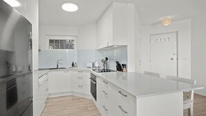 A modern kitchen with white cabinetry, a central island, and a built-in oven. - Ocean Waves - boasting beautiful beach views (Nambucca Heads)