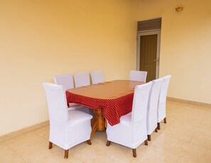A round table with a red and black checkered tablecloth, surrounded by six white chairs with wooden legs.