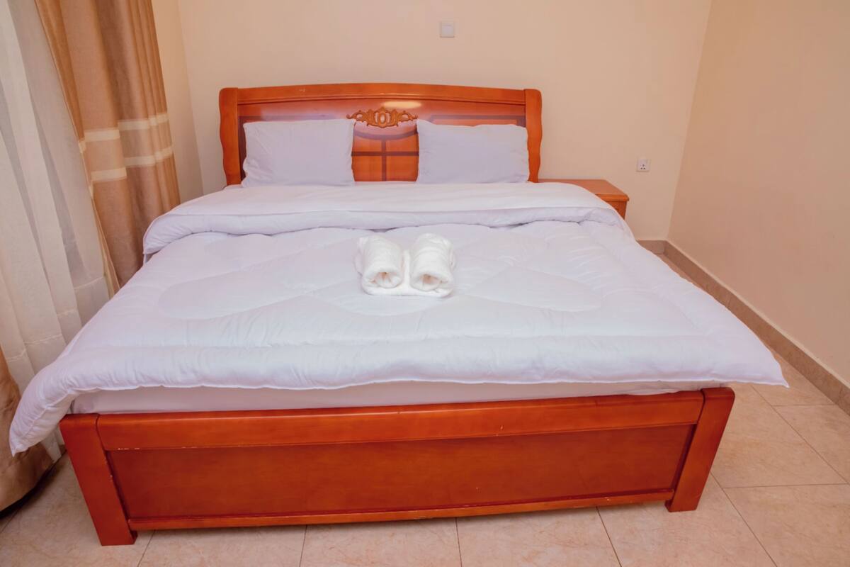 A neatly made bed with a wooden headboard, white linens, and two towels placed on the bed.
