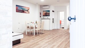 Una cucina moderna con mobili bianchi, un'area pranzo con tavolo e sedie, e un corridoio che conduce a una camera da letto.