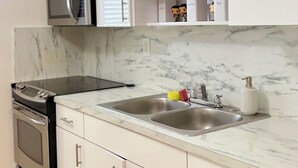A modern kitchen with white cabinets, a stainless steel sink, a microwave, and a built-in oven. - Charming house in terrific Miami with AC, WiFi (North Miami Beach)