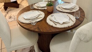 A dining table set with placemats, plates, and cutlery, surrounded by chairs, in a room with a sofa and curtains. - Charming house in terrific Miami with AC, WiFi (North Miami Beach)