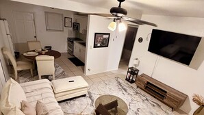 A compact living space with a sofa, ottoman, dining table, and a TV mounted on the wall. - Charming house in terrific Miami with AC, WiFi (North Miami Beach)