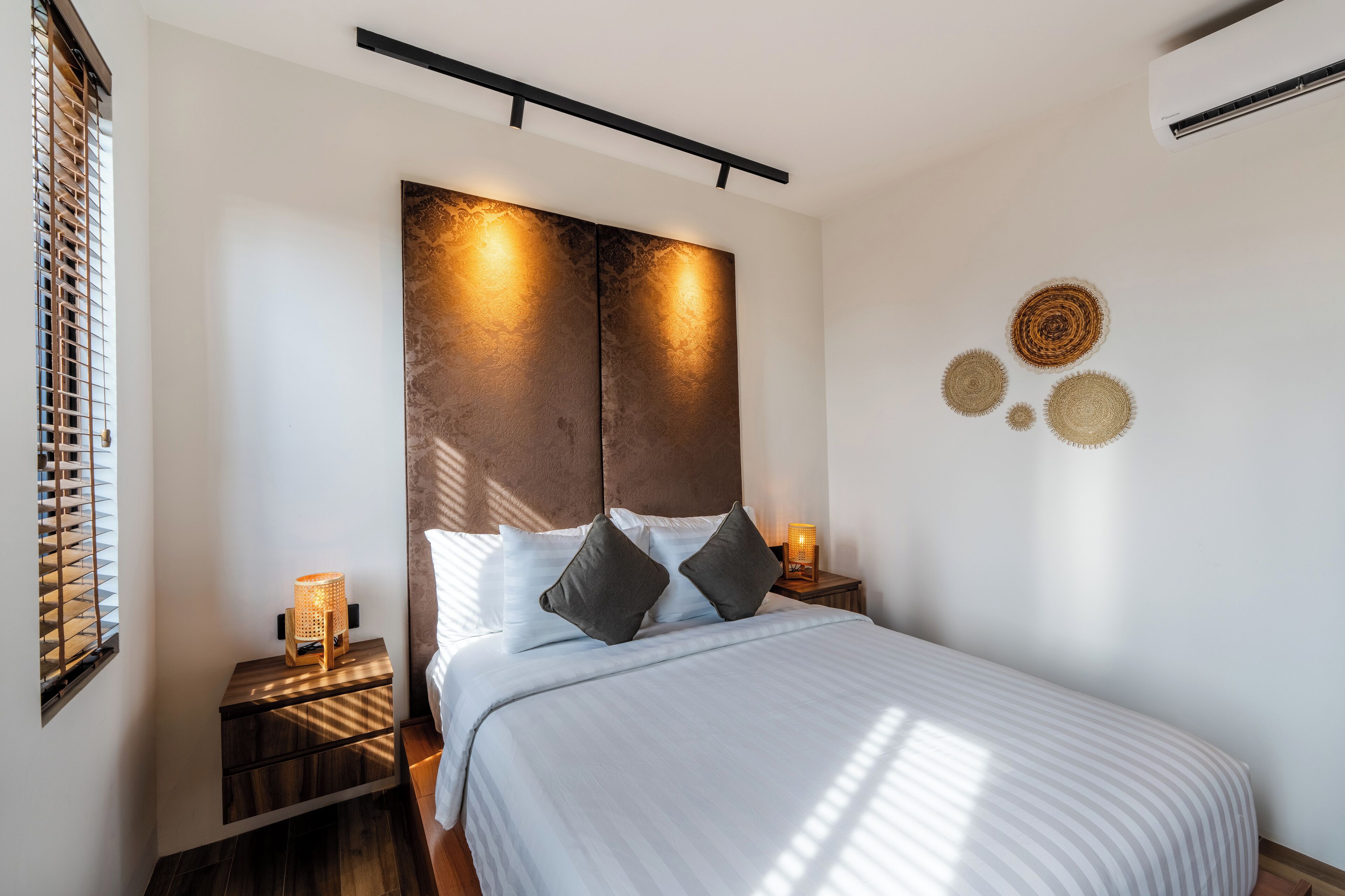 Une chambre à coucher moderne avec un grand lit, une tête de lit à la finition texturée, des lampes de chevet et des œuvres d’art décoratives au mur.