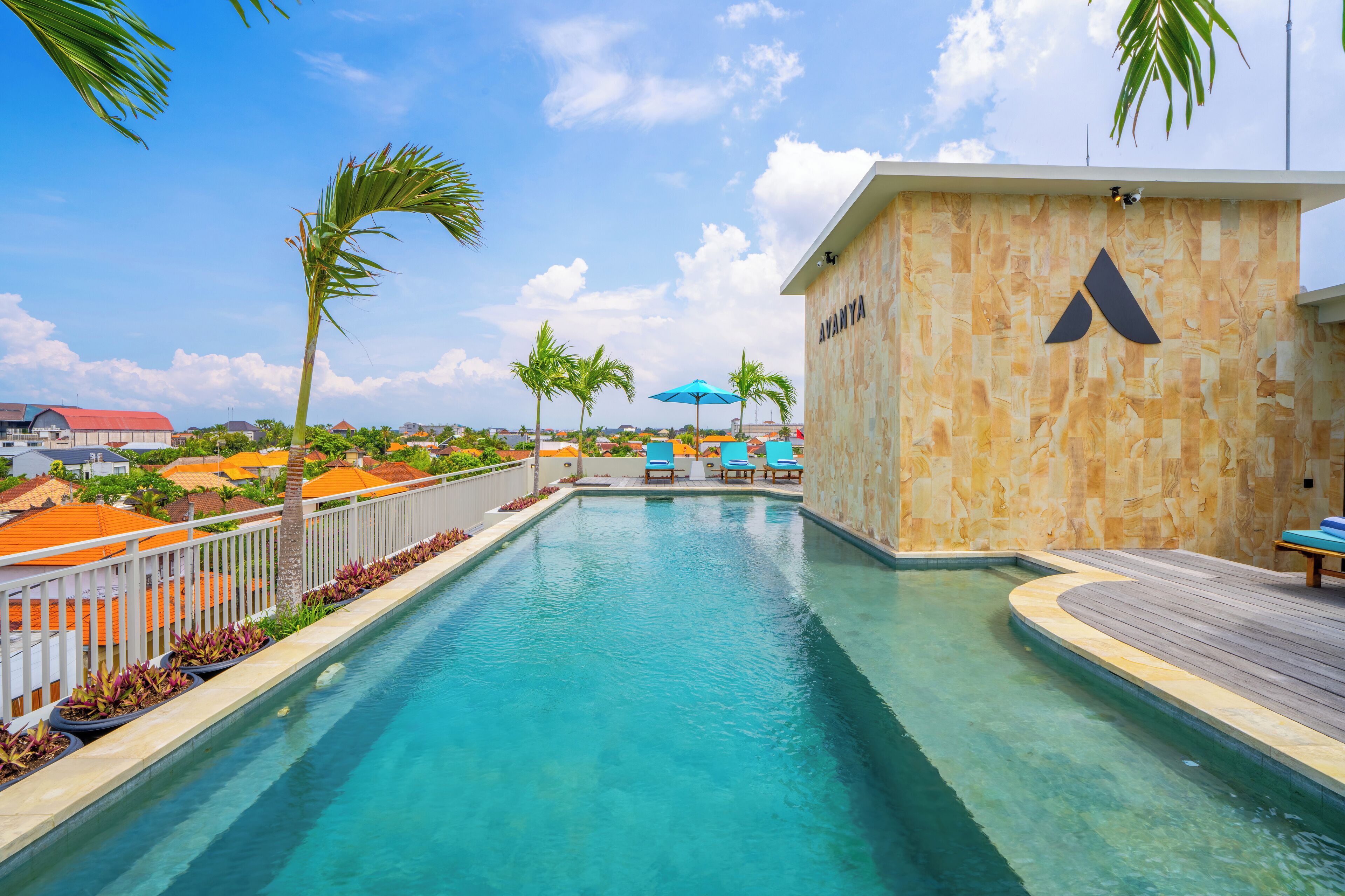 A swimming pool with a wooden deck, palm trees, and a building with a stone facade.
