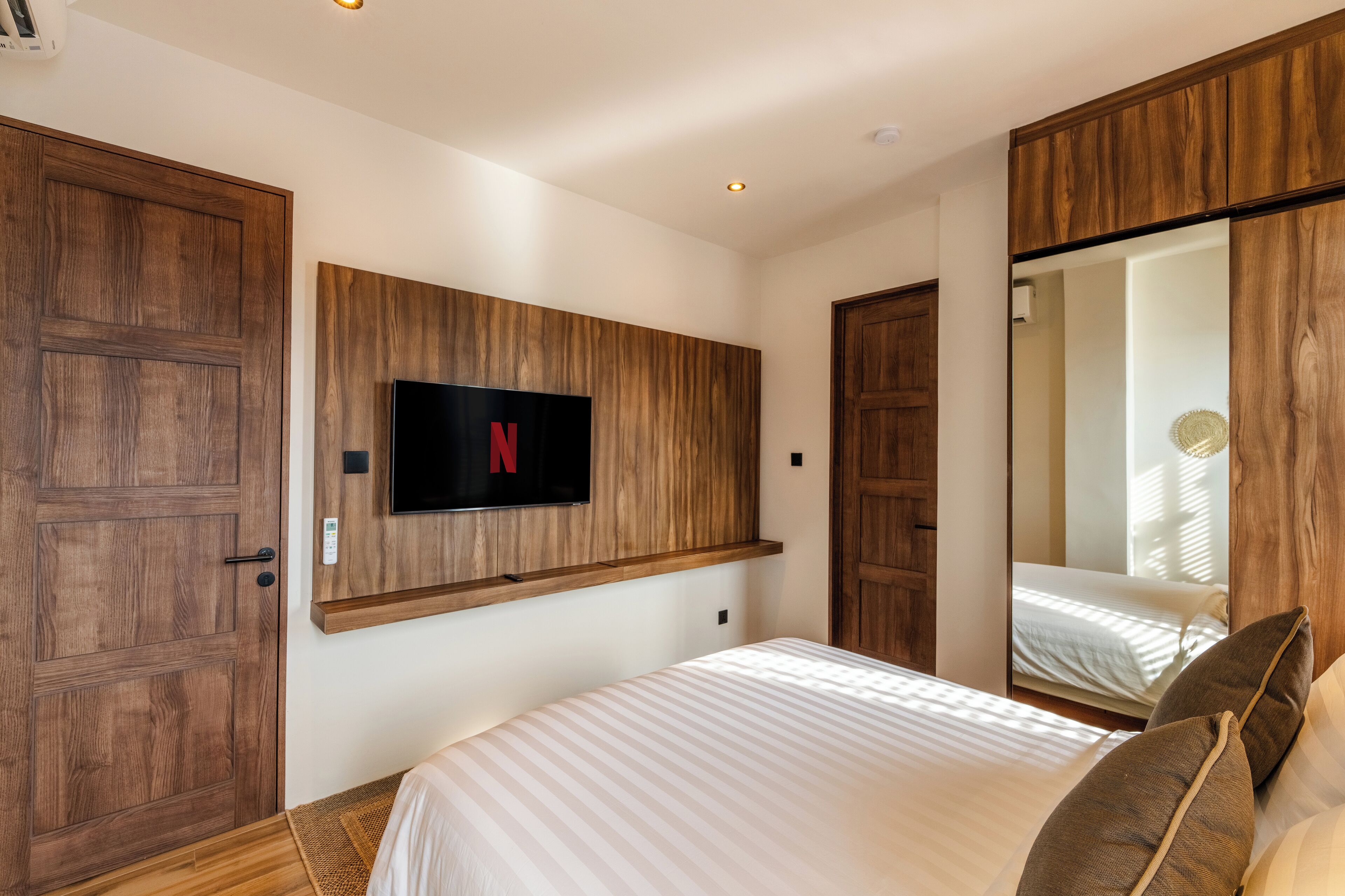 Un dormitorio con una cama grande, un armario de madera y un televisor montado que muestra el logotipo de Netflix.