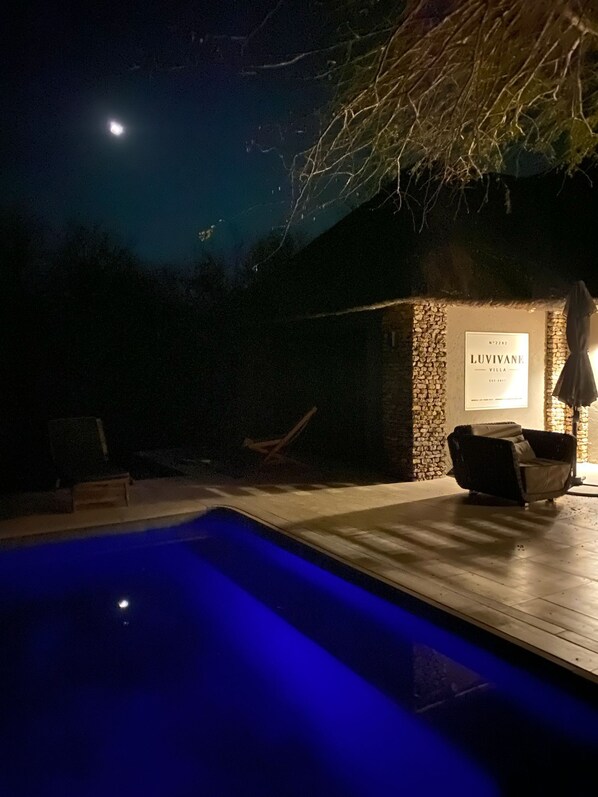 Zona de piscina nocturna con pared de piedra y un cartel que dice 'Luvivane Villa'.