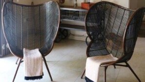 Una habitación con dos sillones de mimbre, un espejo grande y una mesita de noche con lámparas.