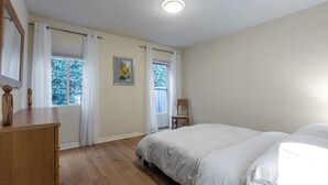 A bedroom with a wooden dresser, a bed with white bedding, two windows with white curtains, and a ceiling light. - Melrose Village Charmer. Walk to world famous shopping and restaurants. (Los Angeles)