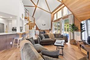 A spacious living area with a large sofa, a coffee table, and a TV. There is a kitchen area with modern appliances and a dining space.