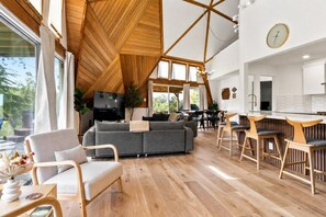 Un intérieur moderne avec un plafond en bois, un canapé gris, des chaises en bois et un coin cuisine.