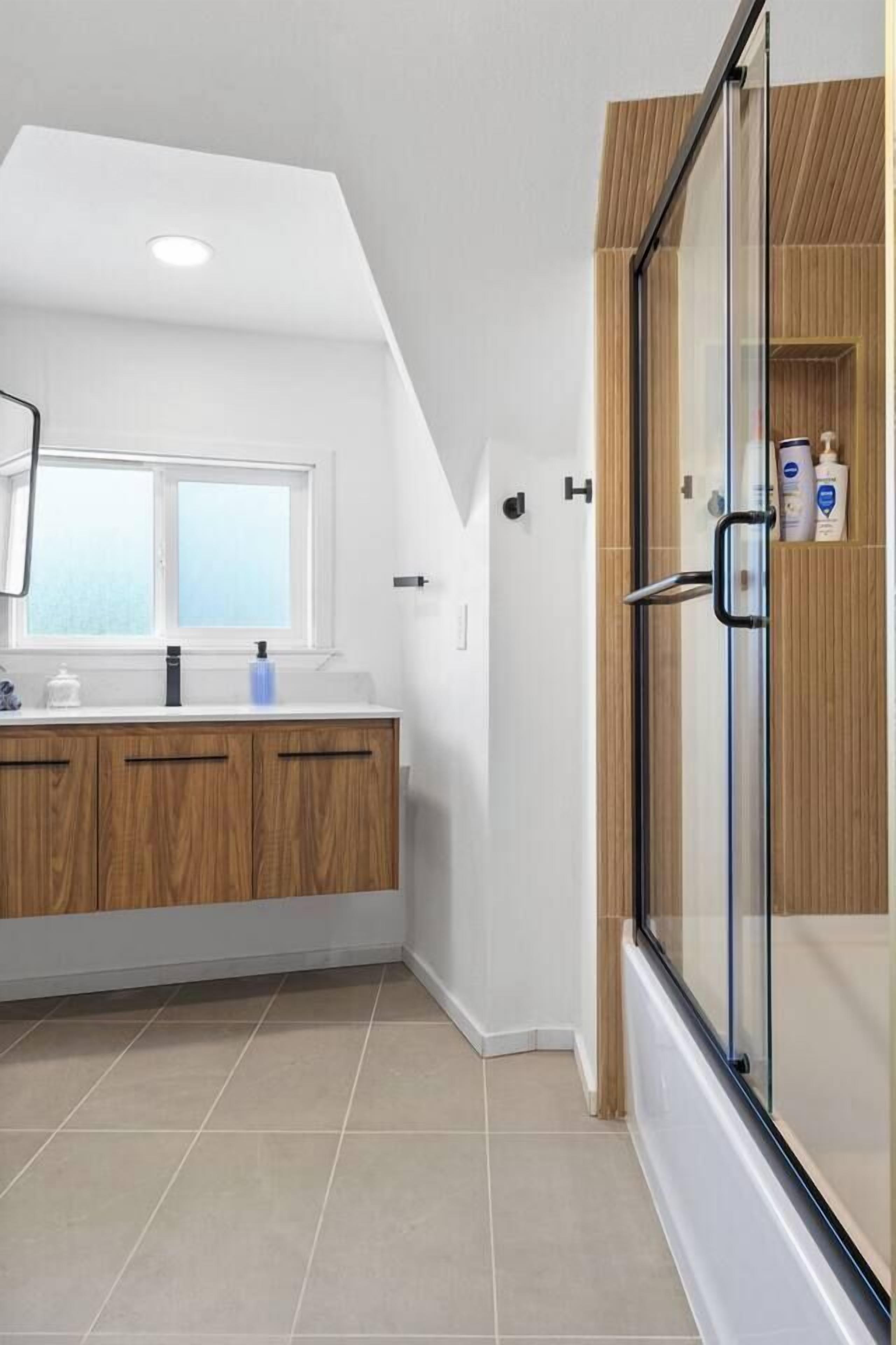 A modern bathroom with a shower enclosure, a window, and a vanity with wooden cabinets.
