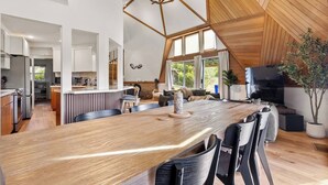 Una cocina amplia con una encimera de madera larga, un comedor con sillas, un televisor y una planta en maceta.