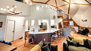 Un loft amplio con techo alto, una isla central con taburetes de bar, una zona de cocina y una escalera que lleva a un nivel superior.