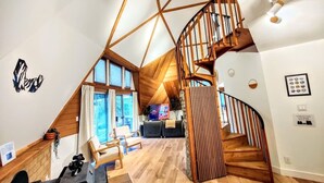 Un interior moderno con una escalera de madera, una sala de estar con sofá y sillones, y un amplio ventanal.
