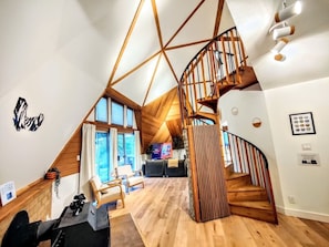 Ein modernes Interieur mit einer Holztreppe, einem Wohnbereich mit Sofa und Sesseln sowie einem großen Fenster.