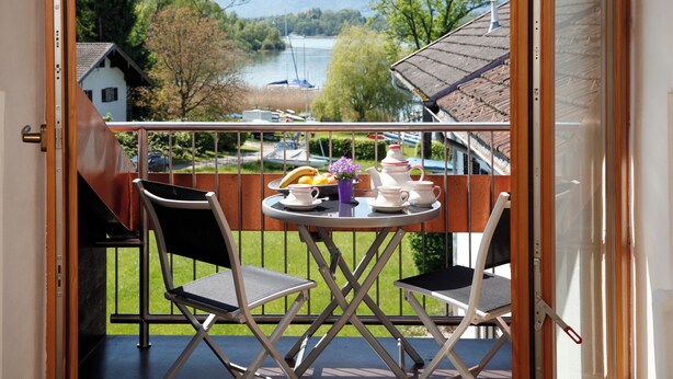 Un balcón con una mesa dispuesta para té, sillas y vistas a un lago y montañas.