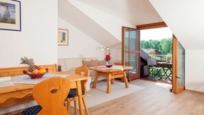 A dining area with wooden furniture, a table with a fruit bowl, and a view of a garden through a glass door.