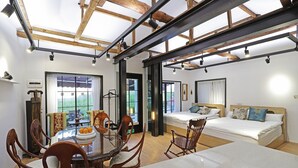A modern room with a wooden ceiling, a bed, a dining table with chairs, and a view of the outdoors.