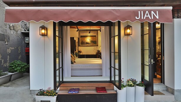 A hotel entrance with a red awning, a wooden bench outside, and potted plants.