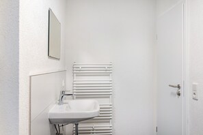 Un baño con lavamanos blanco, un espejo, un perchero para toallas y una puerta.