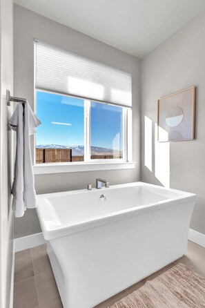 Un baño moderno con una bañera grande, una ventana con vista a la montaña y un perchero para toallas.