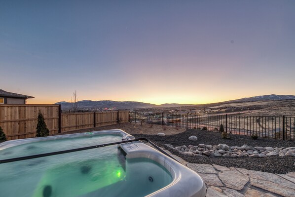 Un jacuzzi en un patio trasero con cerco de madera, vista a montañas y cielo despejado.