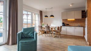 Een moderne woonkamer met een bank, een eettafel met stoelen, een keuken met houten kasten en grote ramen voorzien van gordijnen.