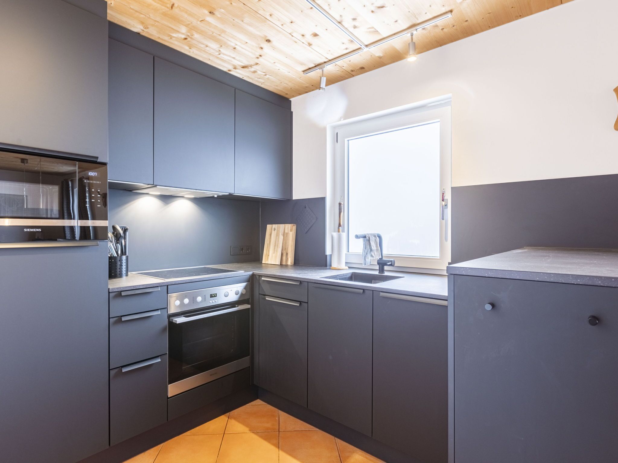 A modern kitchen with grey cabinets, a stainless steel oven, and a window providing natural light.