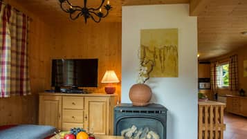 Ein gemütliches Holzhaus-Interieur mit Fernseher, Kamin, Obstschale und einer Chandelier.