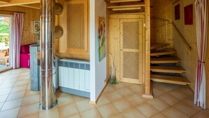 Un interior de madera con un calentador central, una escalera y una puerta con un panel decorativo.