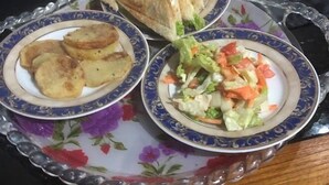 A tray with three plates of food, including sandwiches, potato wedges, and a salad.