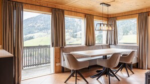 Interior de madera con una mesa de comedor, sillas y grandes ventanales que ofrecen vistas a la montaña.