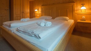 A double bed with white linens and rolled towels, wooden walls, and two bedside lamps.