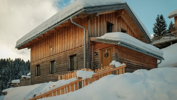 A wooden cabin with a snow-covered roof and a wooden fence in front.