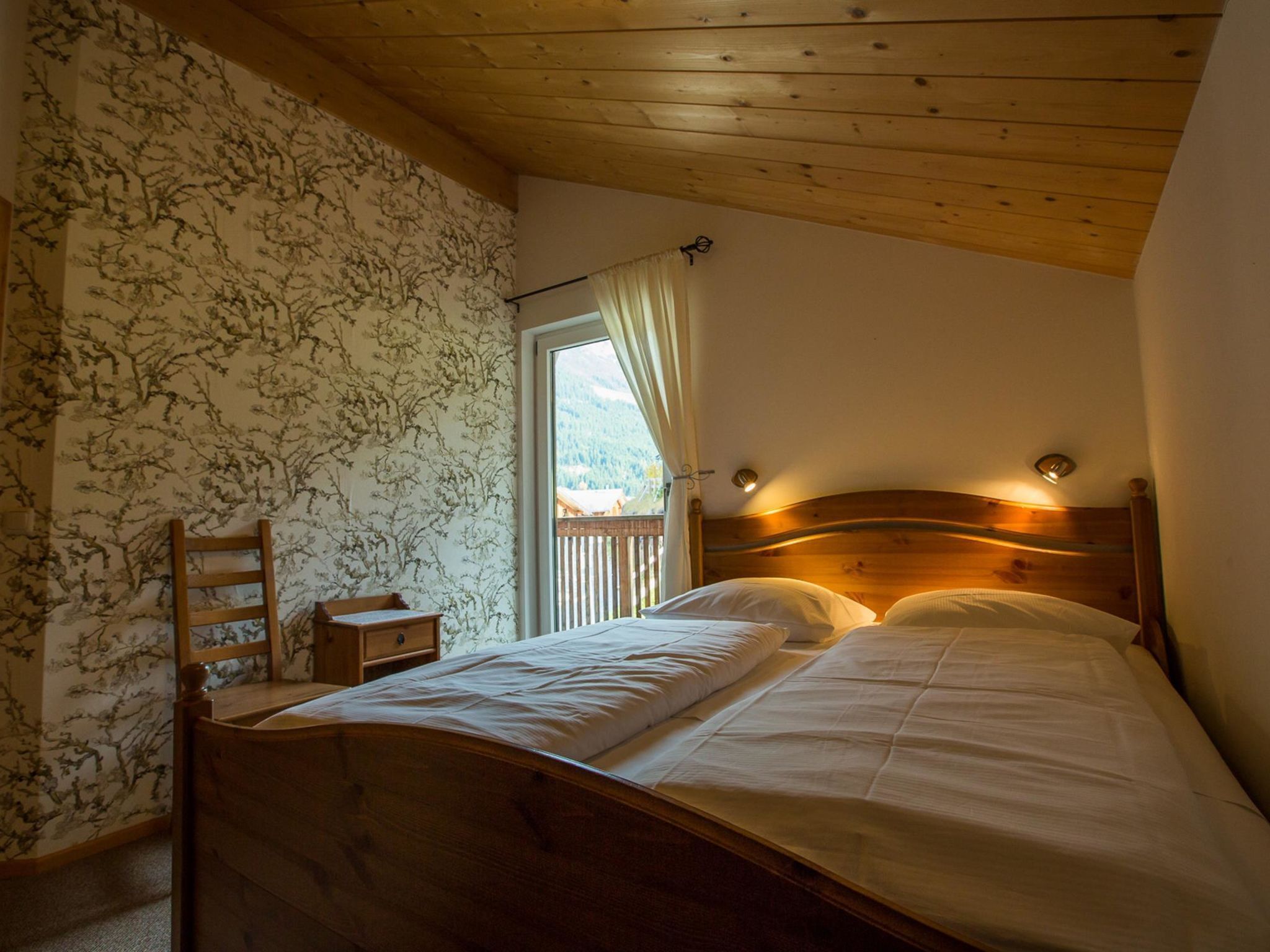 A bedroom with a wooden bed, a nightstand, a chair, and a window with a view of a mountain.