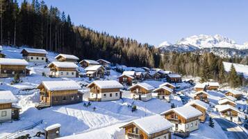 Ein verschneites Dorf mit Holzhäusern, klarem Himmel und einem Berg im Hintergrund.