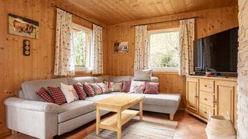 Ein gemütliches Blockhäuschen-Interieur mit einer Couch, einem Holztisch und einem Fernseher.