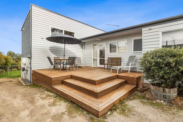 A house with a wooden deck, a patio table with chairs, a bench, and a potted plant.