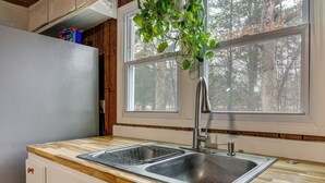 Une cuisine équipée d’un évier à deux bacs, d’un plan de travail en bois et d’une fenêtre donnant sur la forêt.