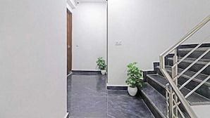A hallway with a marble floor, a staircase with metal railings, and two potted plants. - Hotel Vijaydeep Place Near Delhi Airport (New Delhi)