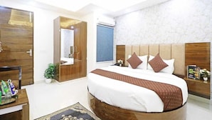 A modern bedroom with a large bed, wooden headboard, and a mirror. There is a desk with a chair and a potted plant. - Hotel Vijaydeep Place Near Delhi Airport (New Delhi)