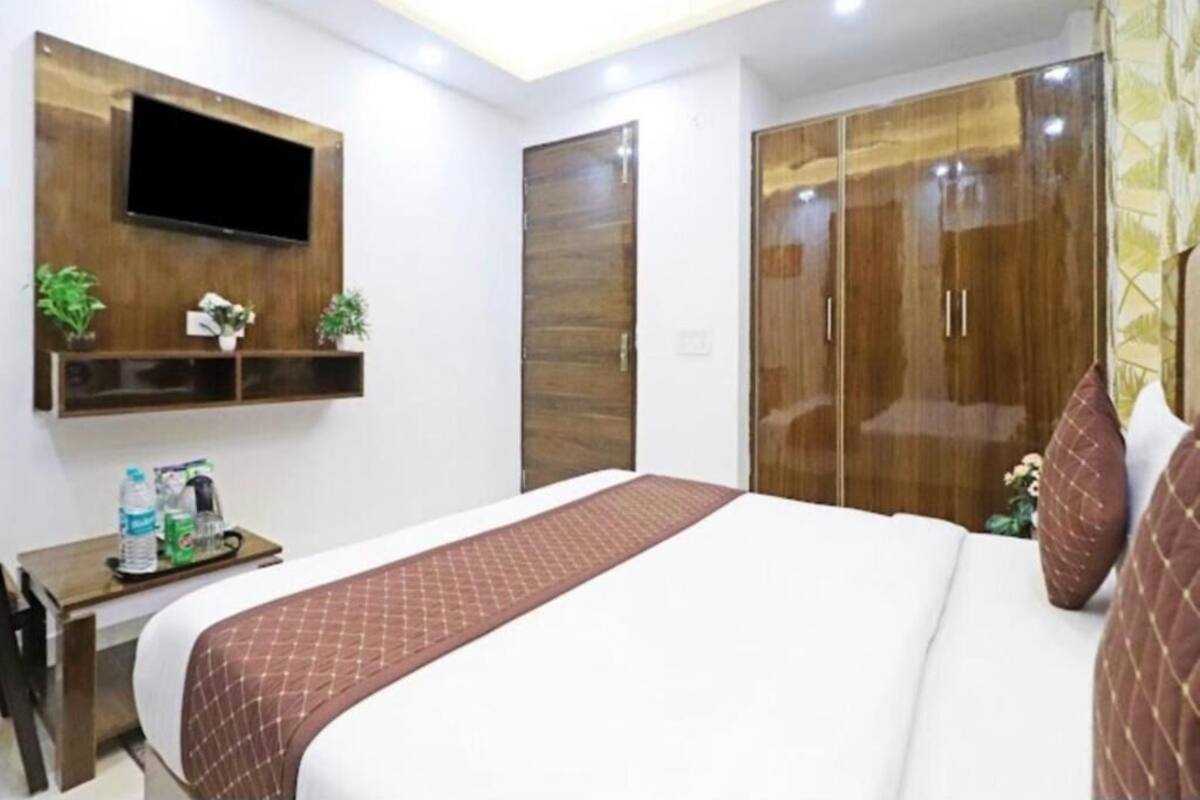 Une chambre d’hôtel avec un lit, un téléviseur fixé au mur, une armoire et une petite table sur laquelle se trouvent une plante et une bouteille.