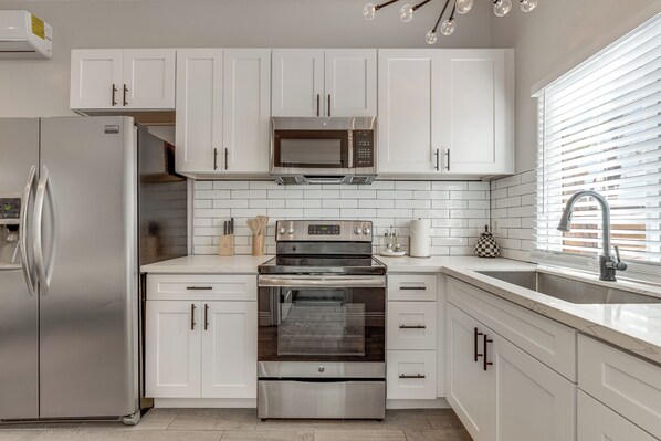 A modern kitchen with white cabinets, a stainless steel refrigerator, a built-in microwave, and an oven.