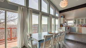 Une cuisine spacieuse avec de grandes fenêtres, un coin repas avec des chaises blanches et une vue sur une terrasse en bois.