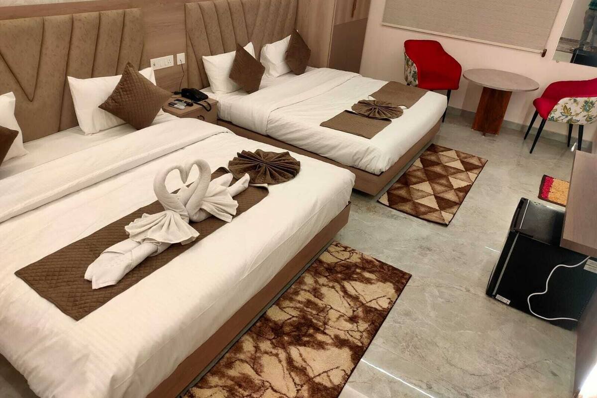 Habitación de hotel con dos camas, cada una con cabecera, almohadas y toallas dispuestas sobre ellas. Hay una mesita redonda y una silla roja en la habitación.