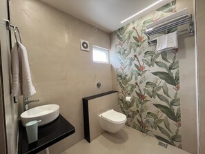 A bathroom with a white sink, a toilet, and a shower area with a floral wallpaper. - Aaditri Inn (Gorakhpur)